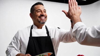 Smiling male chef gives a high-five, celebrating culinary success and teamwork in a professional kitchen, showcasing collaborative spirit and achievement
