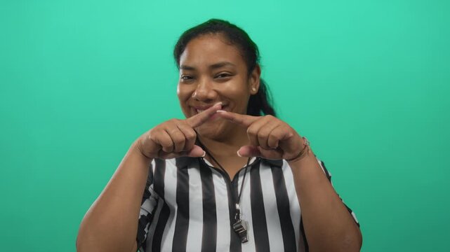 Referee woman in striped shirt blowing kiss with lips and whistle visible to camera in studio; joy affection playfulness.