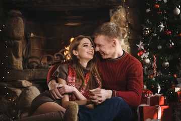 A young couple in love near the fireplace celebrates New Year and Christmas in a romantic atmosphere