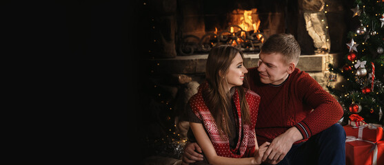 A young couple in love near the fireplace celebrates New Year and Christmas in a romantic atmosphere copy space banner