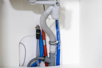 Detailed view of under sink plumbing, revealing a drain hose, red and blue water supply lines, essential for home renovation and repair projects