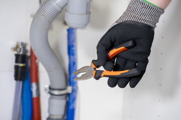 Plumber's gloved hand holding adjustable pliers near complex water pipes, ready for skilled repair and urgent maintenance work