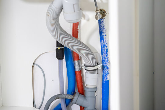 Plumbing connections with corrugated drain hoses, insulated water pipes, and cables hidden inside a cabinet, vital for domestic utility function