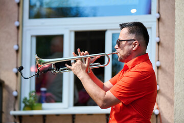 Obraz premium Adult man playing trumpet outdoors in bright daylight near window