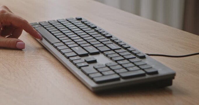 Close up of a hand pressing the space bar on a computer keyboard placed on a wooden desk, with a blurred background of an office or home. Slow motion.