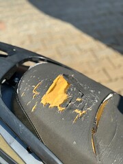 Ripped motorcycle seat with visible damage and exposed foam, suitable for background use