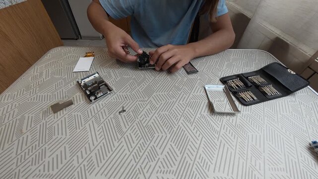 Child repairing small electronic device at table using screwdriver and tools. Hands-on learning, technology curiosity and home electronics repair concept in indoor setting
