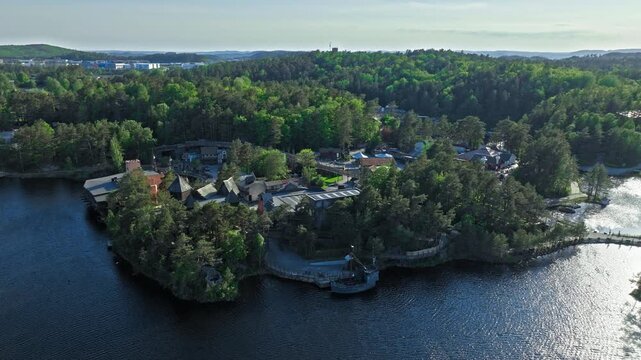 Aerial view of Abra Havn peninsula and forest surroundings. Drone footage of the themed harbor village surrounded by trees and water at Dyreparken in bright summer light..