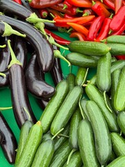 Fresh vegetables market display featuring cucumbers, eggplants, and red peppers on green surface