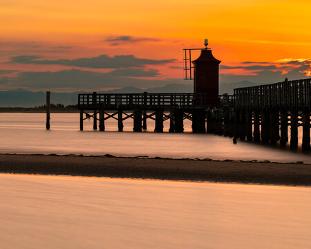 Vertical view of Faro Rosso lighthouse at dawn in Lignano Sabbiadoro, red beacon on pier with long exposure smoothing the Adriatic Sea, minimalist seascape with copy space, Italy travel concept.