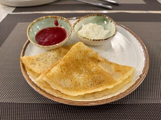 Crepes with sour cream and raspberry sauce served on plate in dining setting