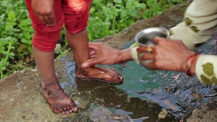 A village woman washes a child’s feet with water outdoors in an Uttarakhand village. The moment reflects poverty, hygiene practice, care, and simple rural mountain life.