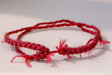 Close-up of a hand-woven crimson bracelet with textured knots. Natural daylight highlights the silk fibers and traditional weaving technique.