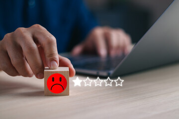 man's hand touches a wooden block with a red sad face icon and a single star, symbolizing extreme dissatisfaction with a poor service experience or low customer feedback ratings