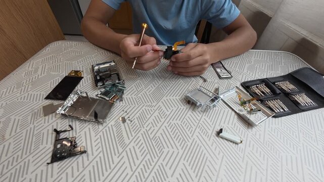 Child repairing small electronic device at table using screwdriver and tools. Hands-on learning, technology curiosity and home electronics repair concept in indoor setting