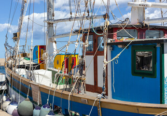 Colorful sailboat docked at a sunny marina in La Caletta, Sardinia, Italy, with clear skies and calm waters.