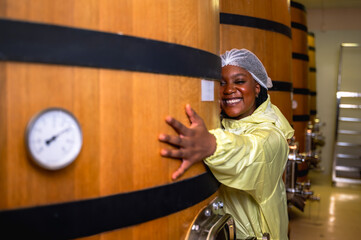 Black female wine making worker working and checking quality from wine fermenting in oak wood barrel underground room