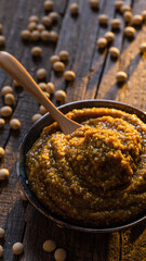 Rustic bowl of traditional Japanese fermented miso paste with wooden spoon. savory food ingredient shows grainy texture from soybeans on an earthy wooden background