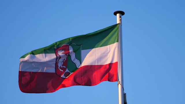 Flag of the state of North Rhine-Westphalia blowing in the wind, blue sky in the background