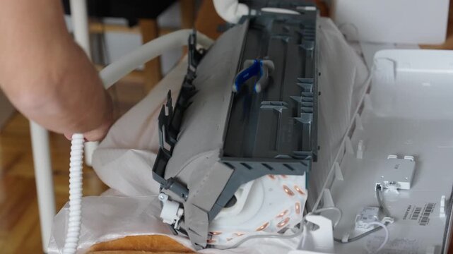 Technician opens split air conditioner indoor unit and adjusts wiring and drain hose. Neutral indoor scene, HVAC installation and maintenance video frame