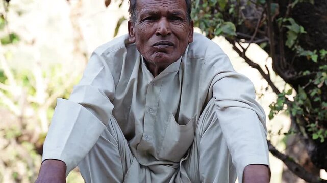 Close up of an elderly Indian village man smoking bidi in Uttarakhand. The scene reflects poverty, rural lifestyle, addiction, daily habit, and simple mountain life in India.