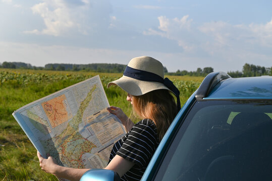 Rear view shot of couple driving on country road. Woman holding map and showing the route map to her boyfriend driving the car. Couple on a road trip.