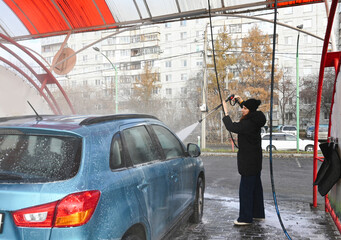 Woman washes her car using a pressure washer at a self-service car wash in the city during a gray day