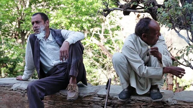 Close up of an Indian village man smoking bidi while resting outdoors in Uttarakhand. The scene reflects poverty, rural lifestyle, addiction, daily habit, and simple mountain life in India.