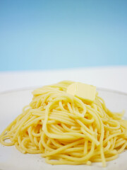 Pile of cooked spaghetti with a butter cube on top, side view on blue and white background, simple comfort food portion of hot pasta for everyday meals