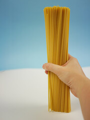 Closeup of hand gripping a bundle of long dry spaghetti pasta in front of soft blue background, simple Italian food ingredient image for cooking themes. Pro Photo