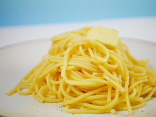 White plate full of cooked spaghetti with a small piece of butter in the middle, top view on neutral background, minimal hot pasta dish for menu design