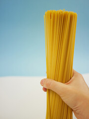 Human hand holding a tall bundle of uncooked spaghetti pasta against blue and white background, food concept of dry Italian noodles and cooking ingredients