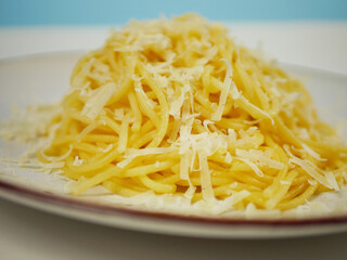 Closeup view of cooked spaghetti covered with grated parmesan cheese on a white plate, warm cheesy pasta portion for Italian comfort food and restaurant menu visuals