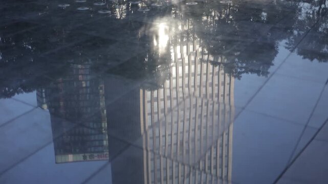 High-rise building reflection in water puddle under golden light and blue sky at sunset