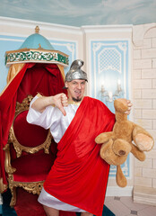 Angry funny man wearing medieval costume showing thumbs down and holding teddy bear