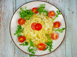Top view of white plate with spaghetti, grated parmesan cheese, fresh arugula and cherry tomatoes on rustic wooden background, colorful Italian pasta salad for menus and blogs