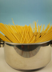 Front view of metal pot filled with upright uncooked spaghetti pasta against blue and white background, minimal Italian cuisine concept with dry noodles and copy space