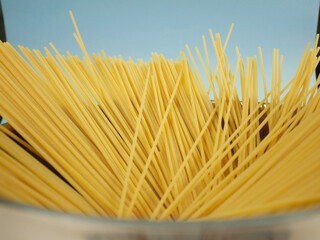 Closeup top edge view of uncooked spaghetti fanned out inside metal pot on blue background, detailed texture of long dry pasta for Italian food concepts