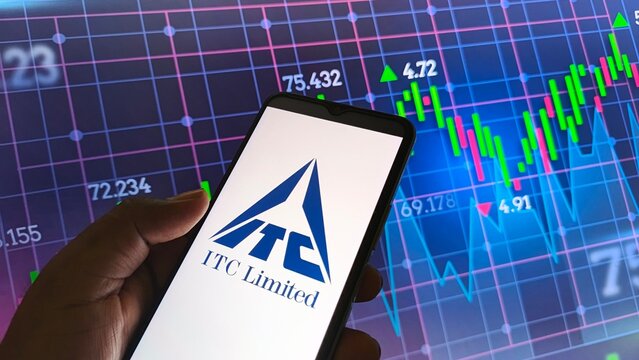 Hand holding smartphone with ITC Limited logo on screen in front of stock market graph