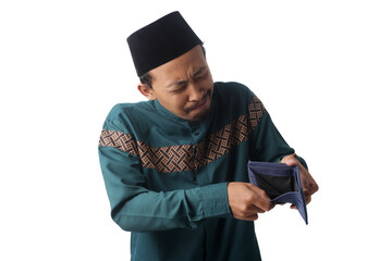 Confused young Asian Muslim man holding an empty wallet with a speechless expression, unsure what to do with no money during Ramadan before the Eid celebration. Isolated on a white background.