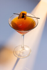Beautiful amber cocktail, a Negroni or manhattan served up on a white surface with dramatic lighting.
