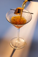 Beautiful amber cocktail, a Negroni or manhattan being poured into a martini glass with dramatic lighting.