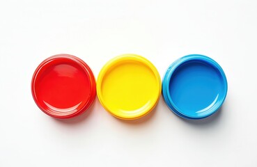 Three open plastic jars of red yellow and blue paint arranged in a row on a clean white surface. Essential art supplies for kids crafting and school projects.