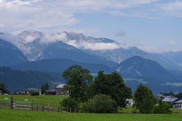 Scenic mountain countryside with open meadows, forested slopes and small rural homes. Calm natural environment, fresh air, travel destination and outdoor lifestyle concept.