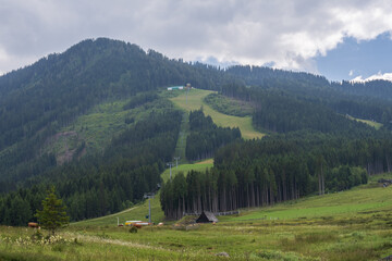 Scenic mountain countryside with open meadows, forested slopes and small rural homes. Calm natural environment, fresh air, travel destination and outdoor lifestyle concept.