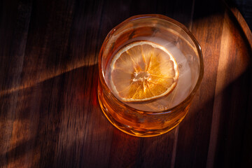 whiskey cocktail served on the rocks garnished with a dehydrated orange slice with dramatic lighting served on a wooden surface.