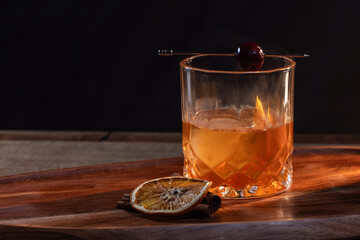 whiskey cocktail served on the rocks garnished with a dehydrated orange slice and a cherry with dramatic lighting served on a wooden surface.
