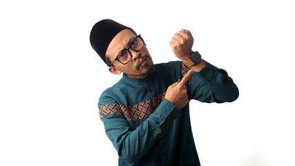 Impatient young Asian Muslim man pointing at his wristwatch while waiting for iftar, the time to break fasting during Ramadan. Isolated on a white background