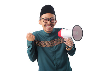 Excited Asian Muslim man holding a megaphone and clenching his fists in a "YES" gesture, celebrating success or achievement. Isolated on a white background. Concept of success, joy, or announcement