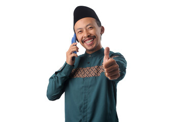 Asian Muslim man in a green traditional outfit giving a thumbs-up gesture to the camera while listening on a phone call, Isolated on a white background. Concept of agreement, good news, satisfaction